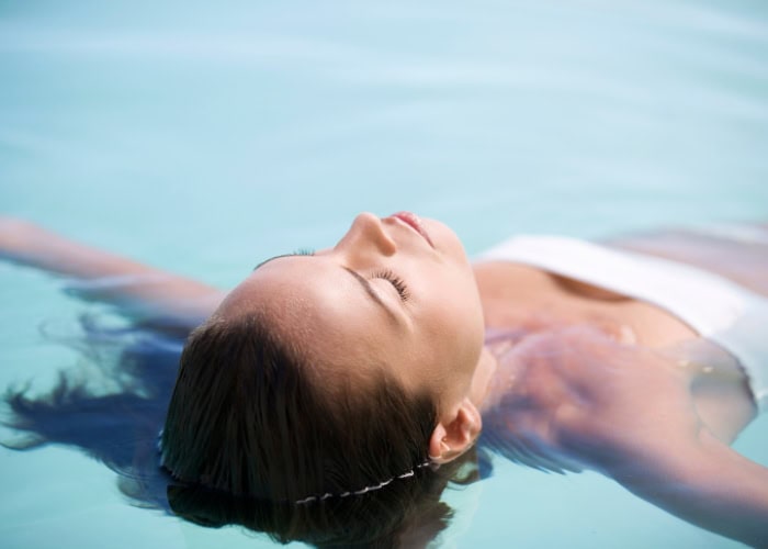 A woman in a white swimsuit is floating calmly in a pool.